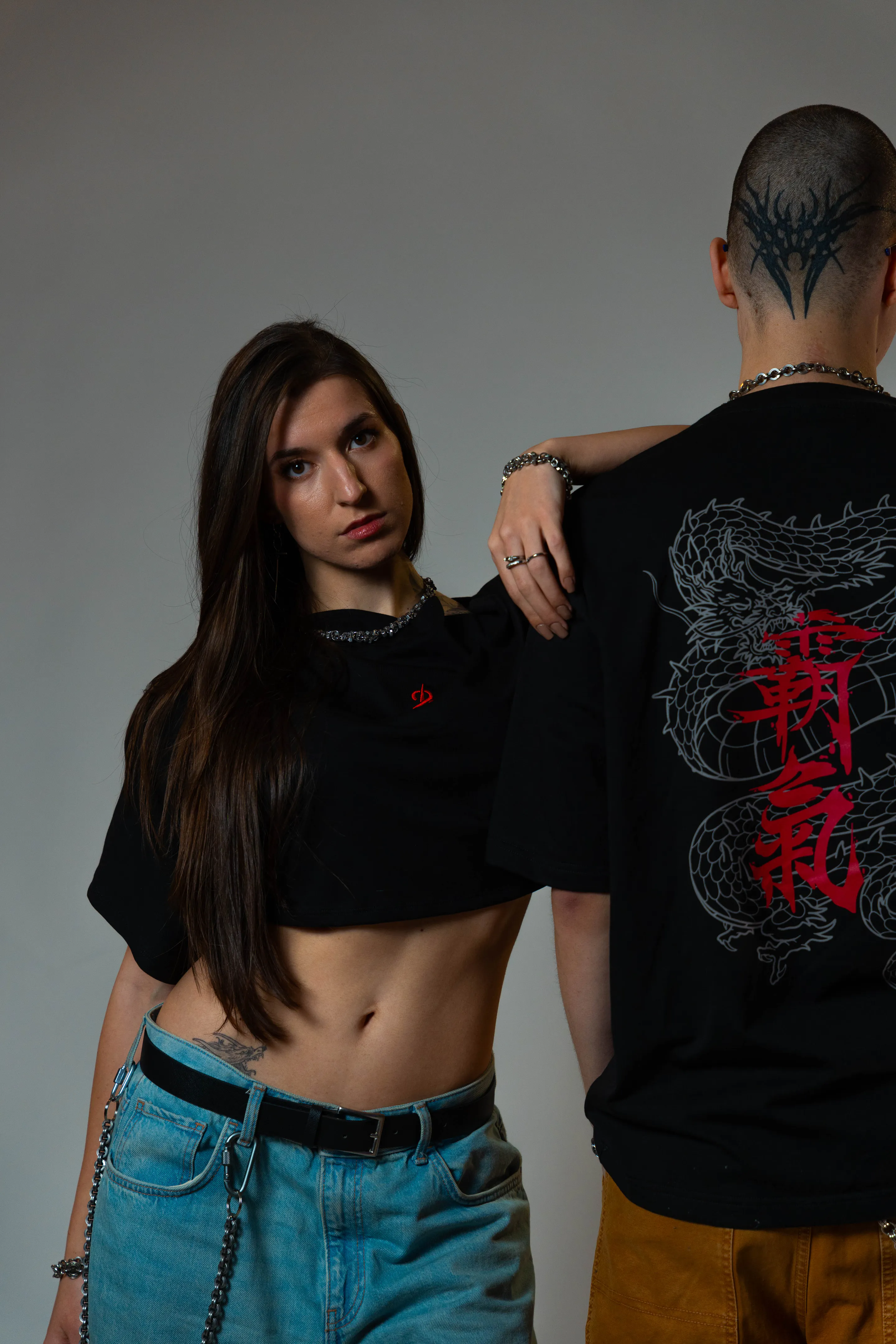 Studio pair — her direct gaze over the dragon-print tee on his back, warm key light