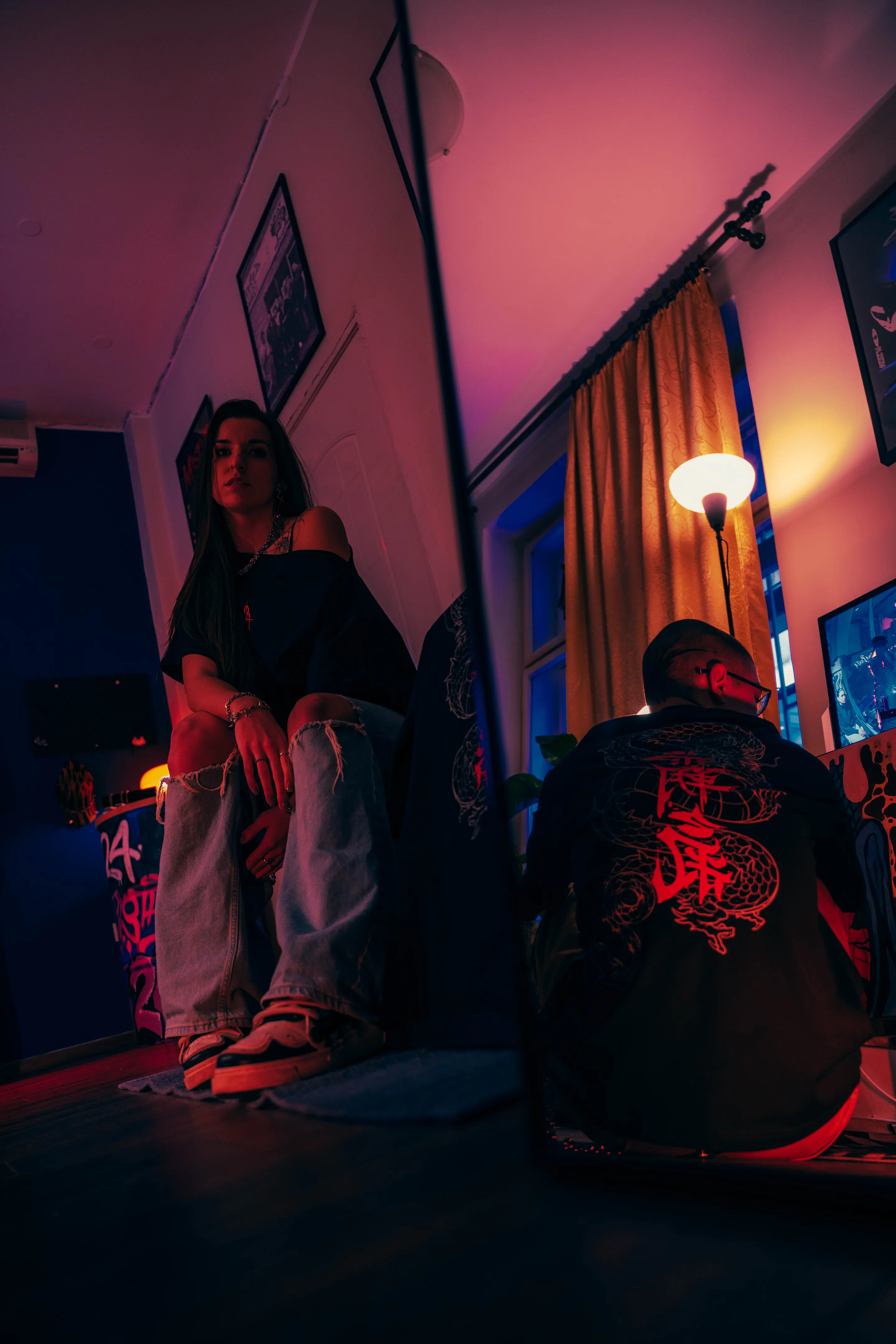 Pink-lit room scene — seated at the bed's edge, the dragon back print turned away at right