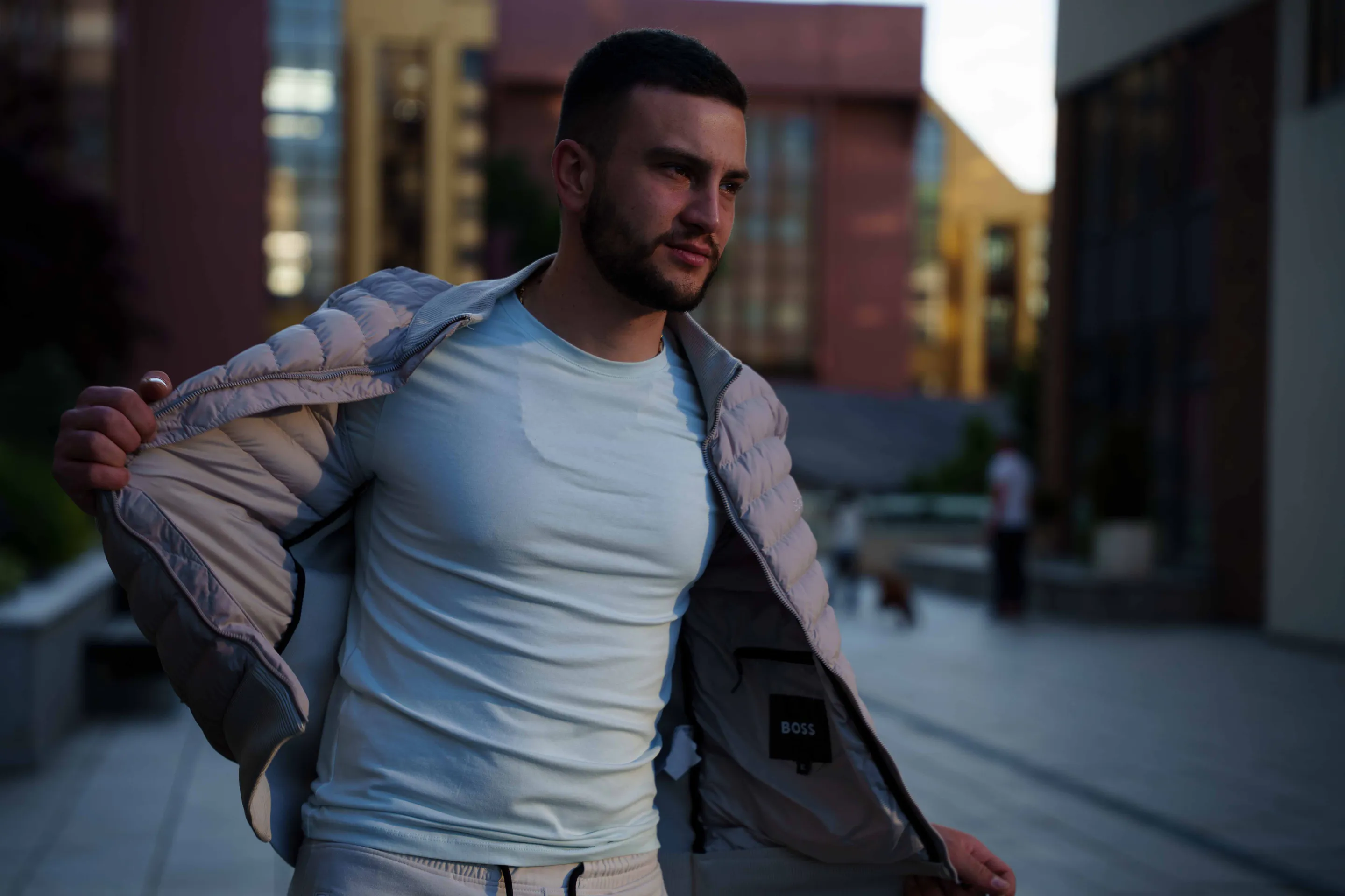 Opening the jacket mid-walk, white tee underneath, last light