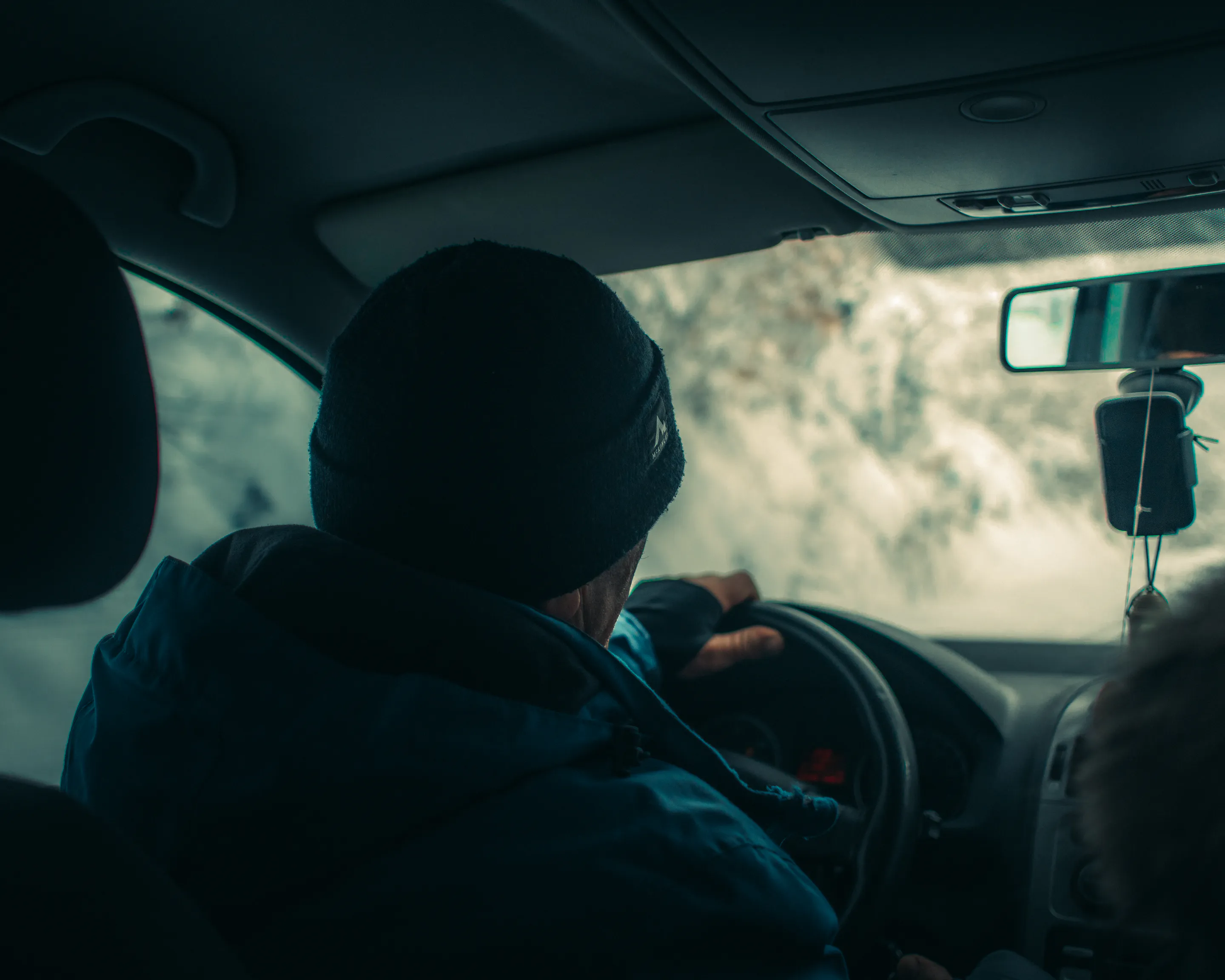 The driver from behind, one hand on the wheel, snow country blurred through the fogged windshield
