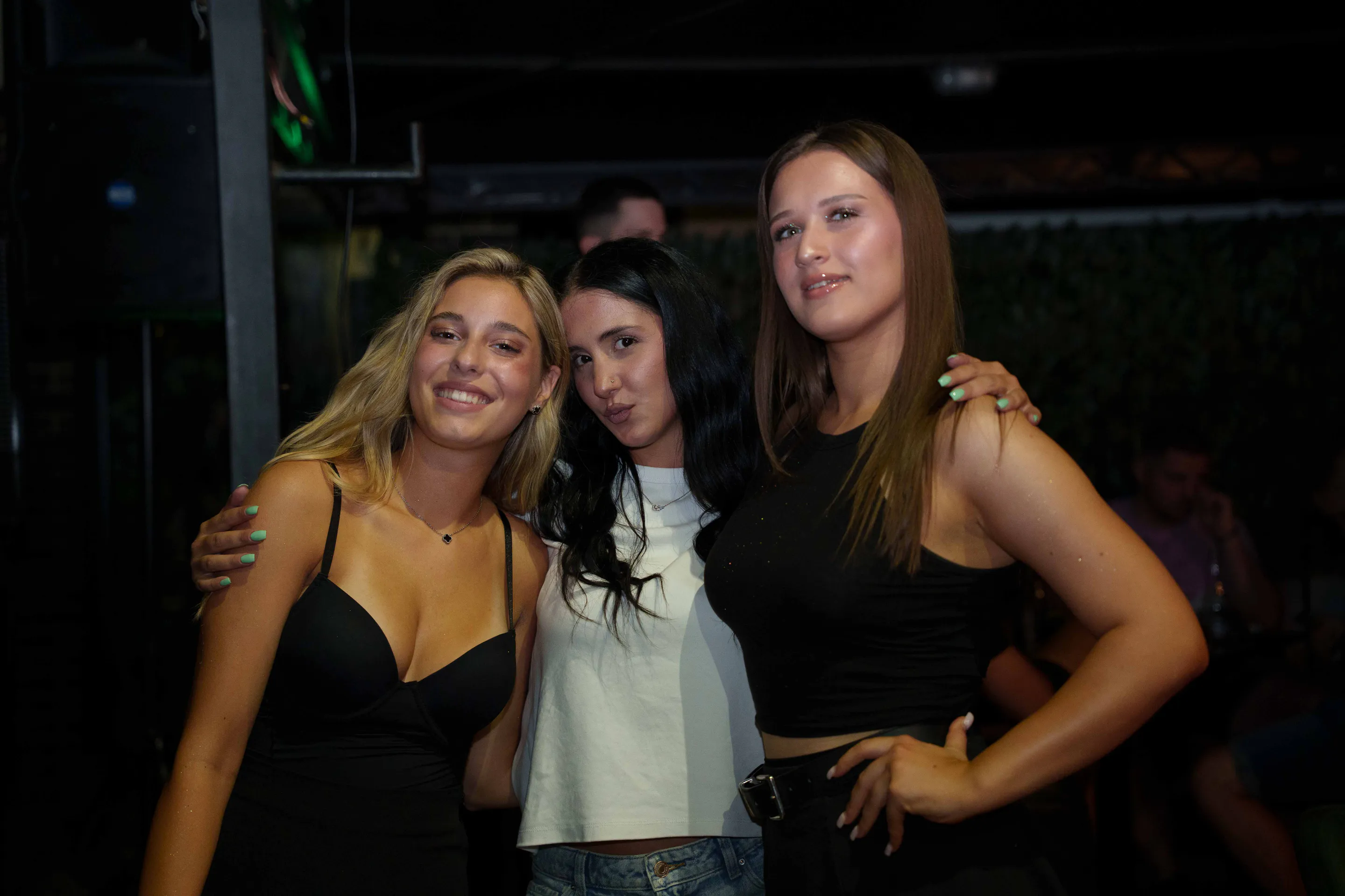 Three friends posing on the terrace, club light grazing past