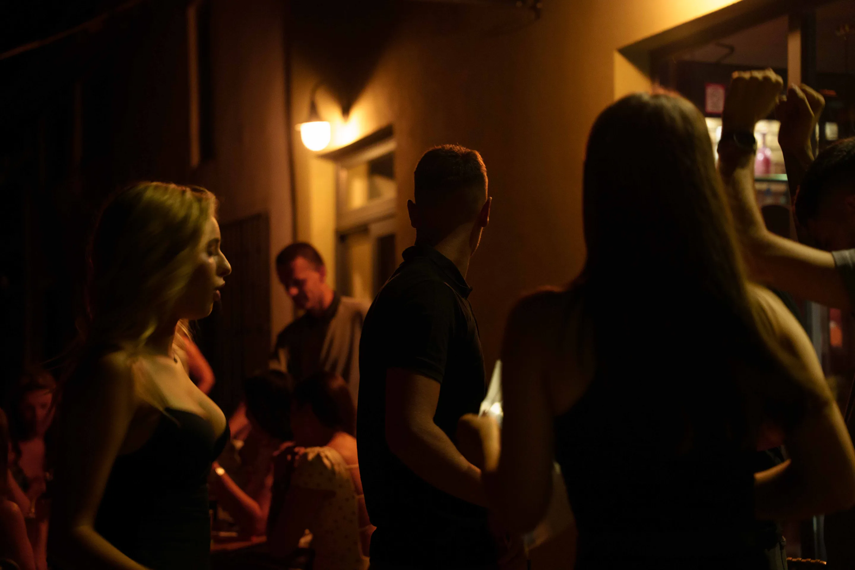 Guests in silhouette against the amber lamplight of the corridor