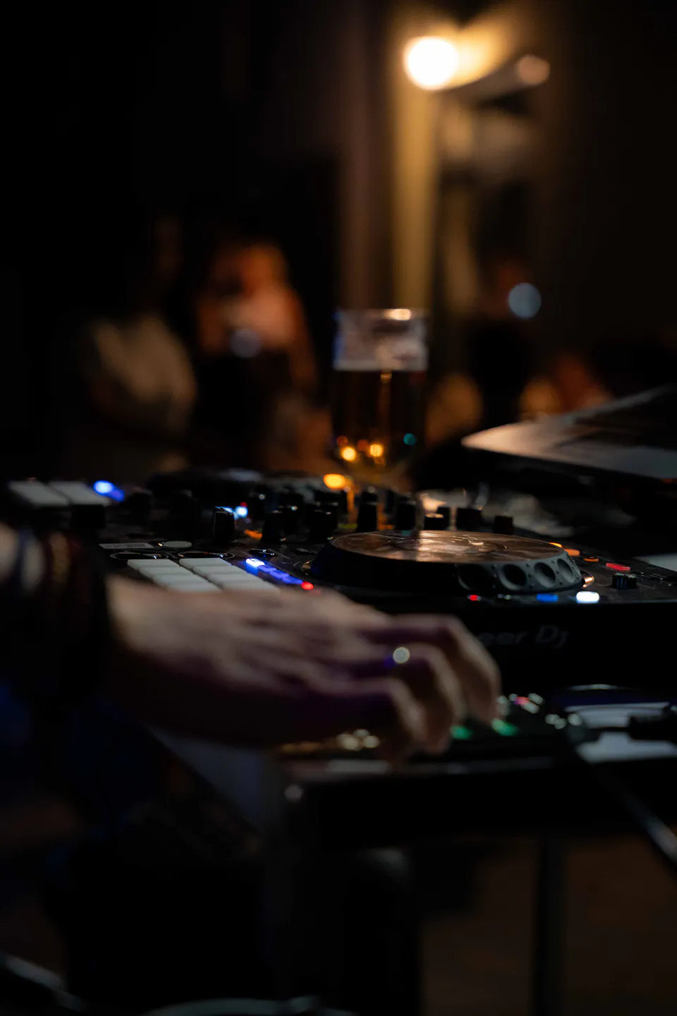Hands on the decks, a lit pint balanced above the mixer