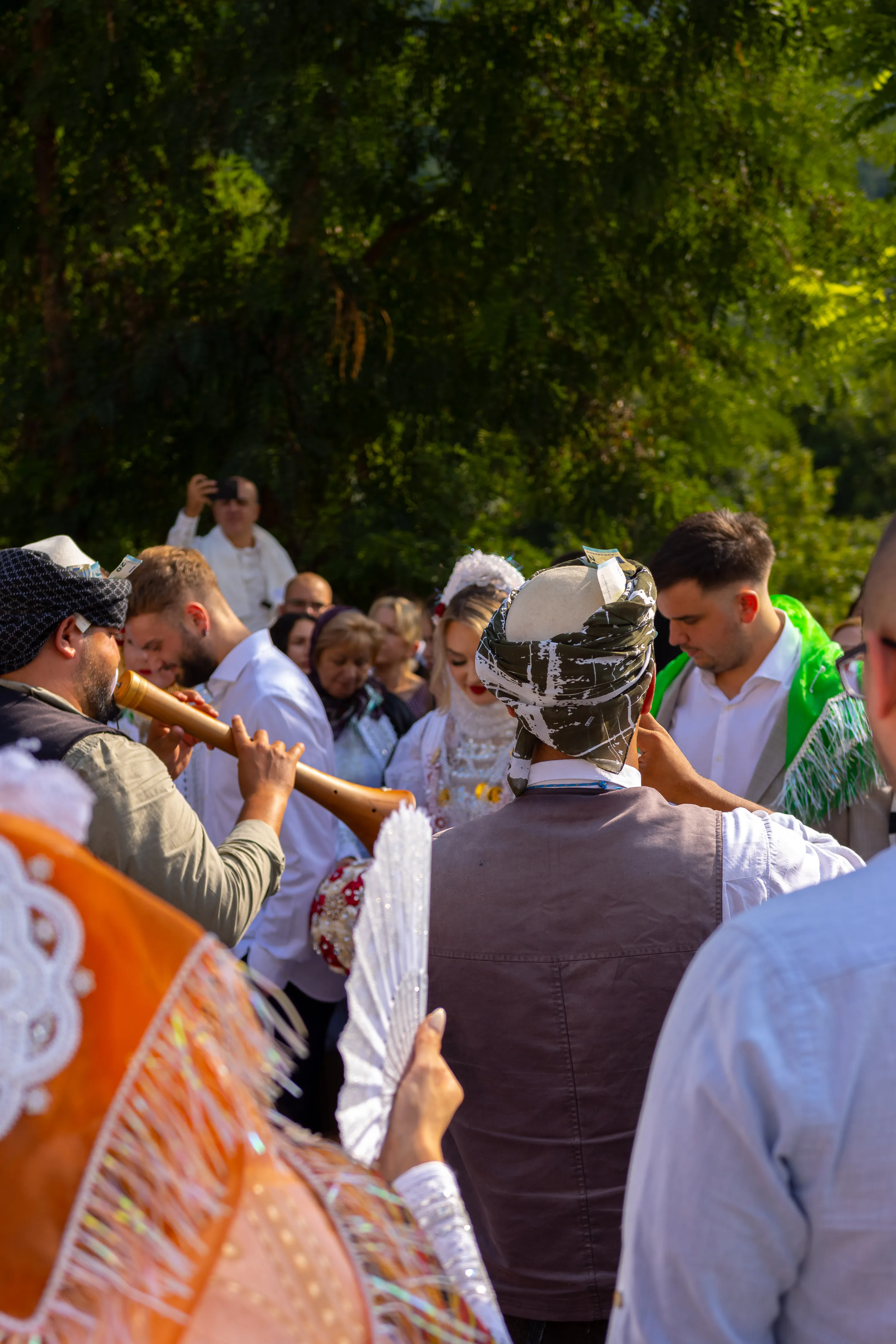 Guests crowd the groom-to-be as a zurna is played straight at him, the green fringed shawl over his shoulders