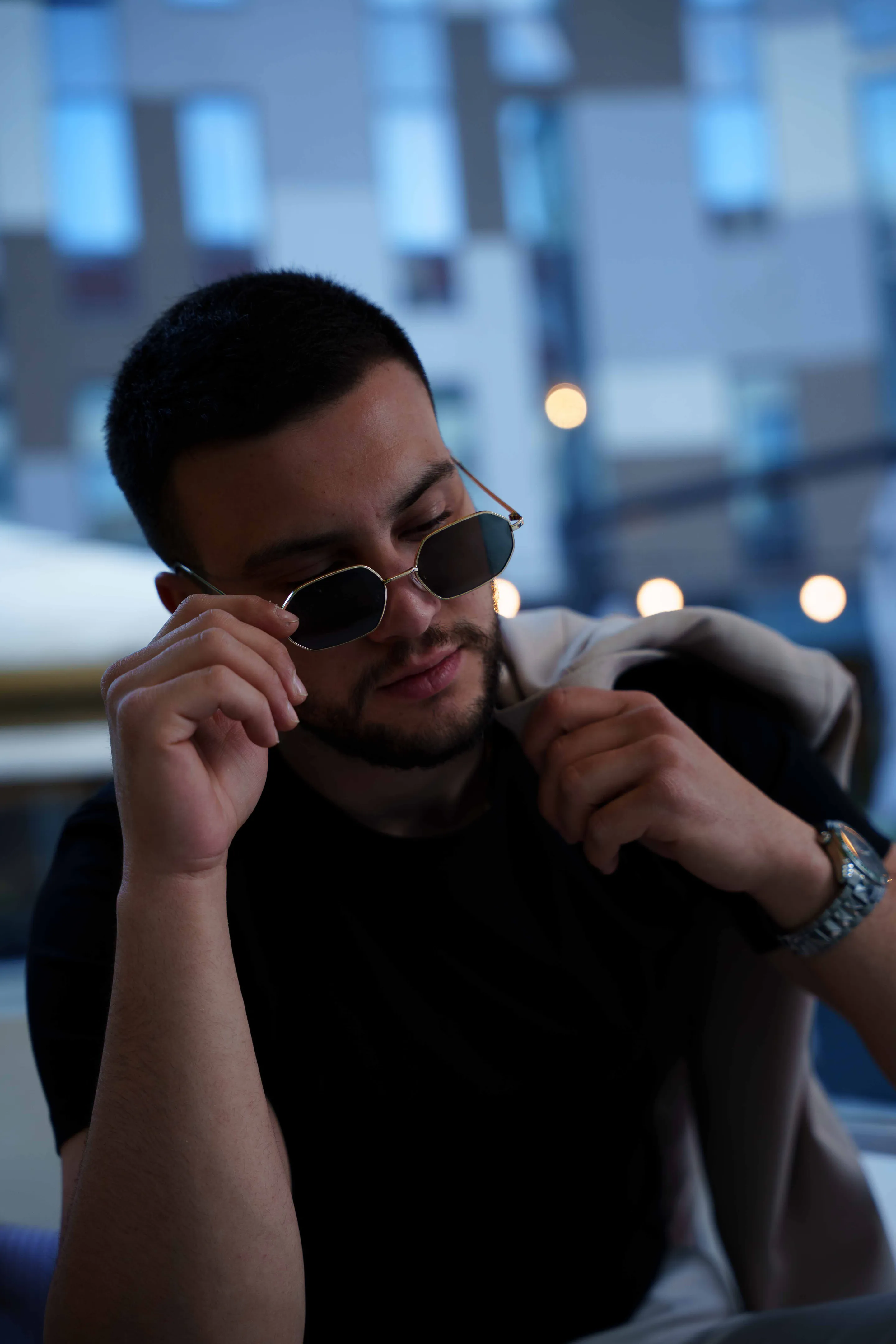 Dusk portrait lowering his sunglasses, glass towers blurred behind