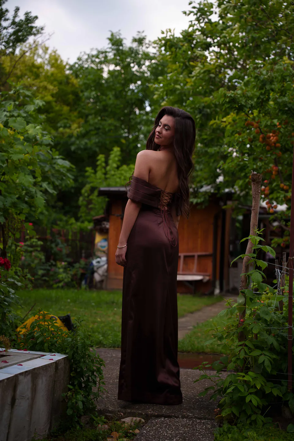 Walking the garden path away from camera, looking back over her shoulder