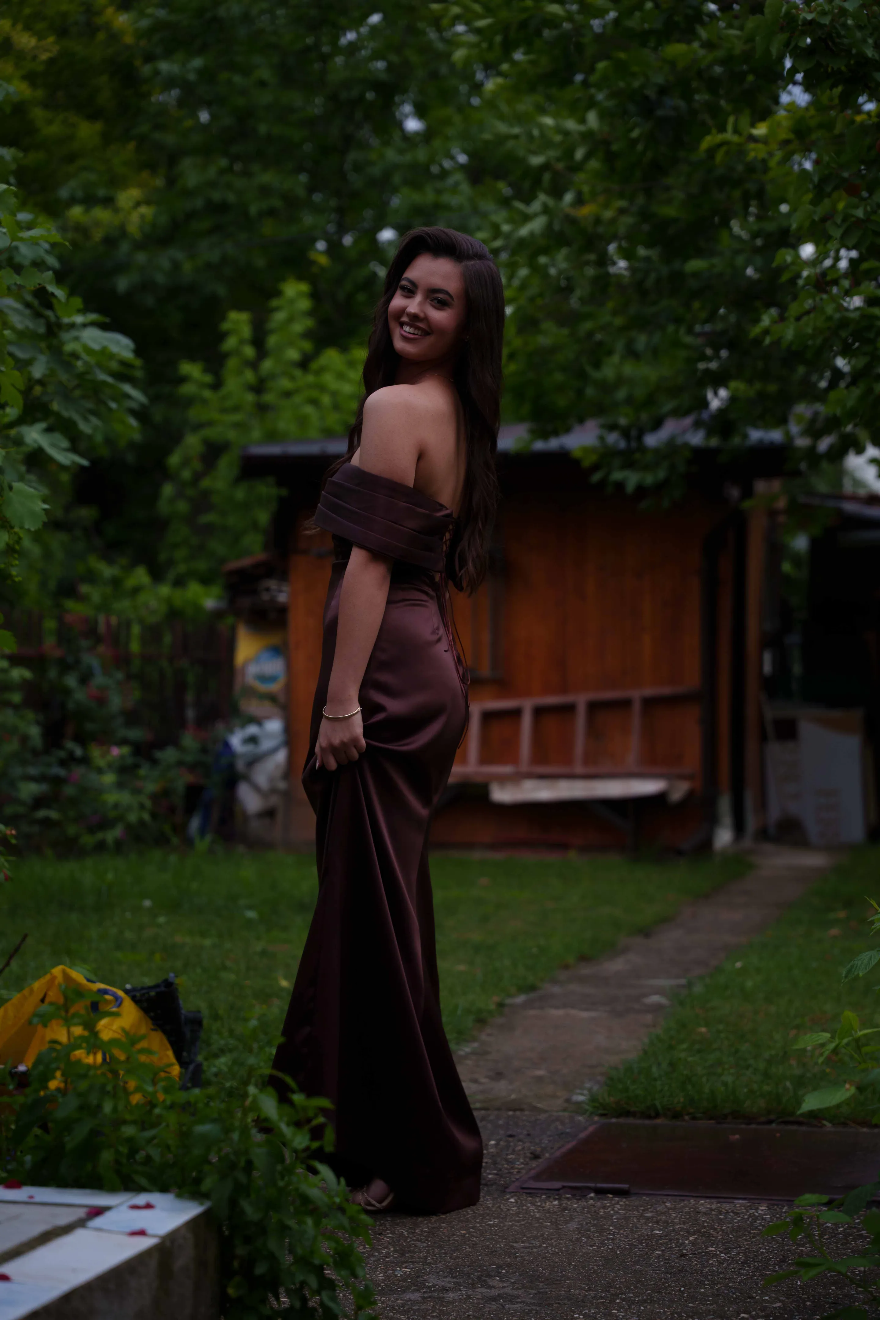 Full-length profile on the path between planted beds, wooden cabins behind