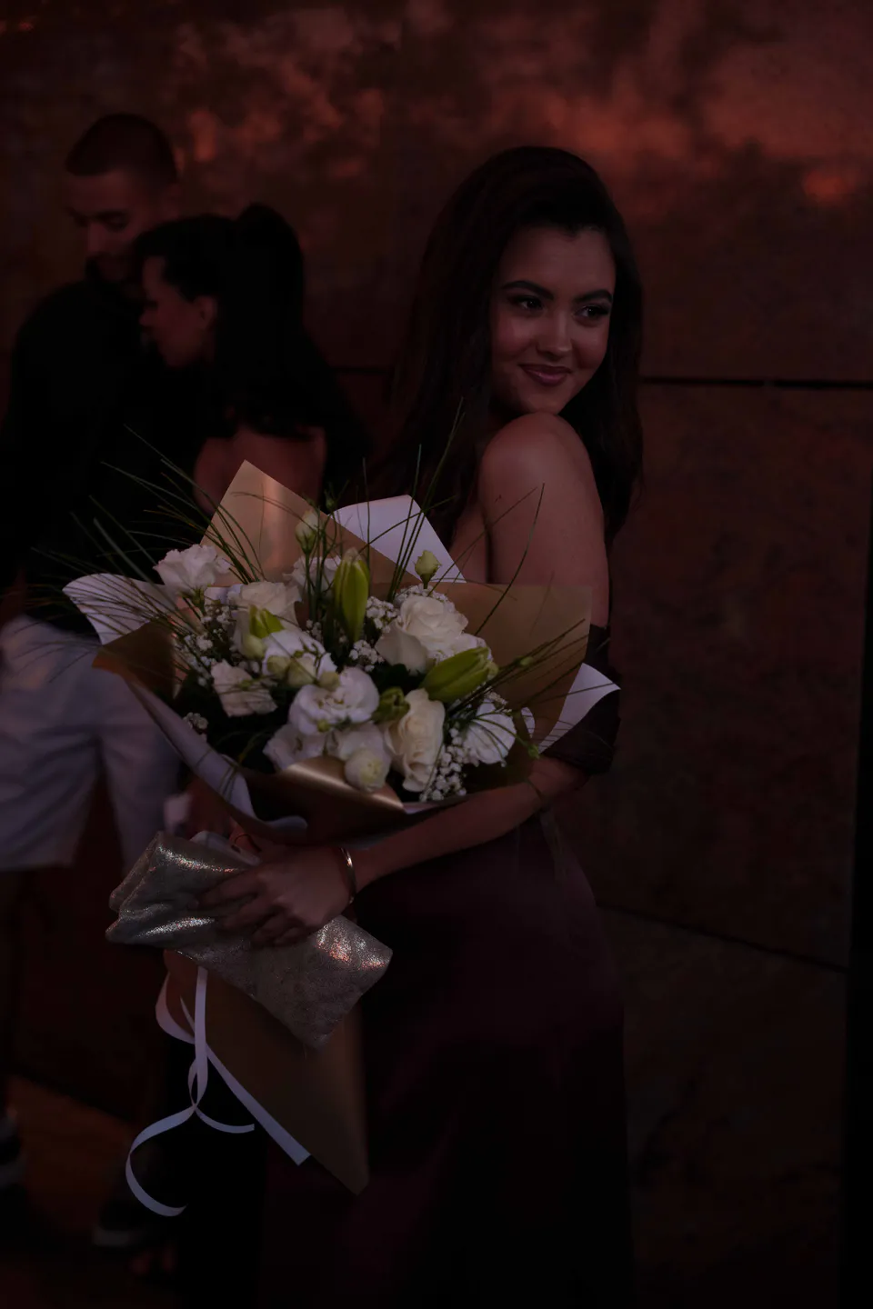Night frame washed in red light, the white bouquet in her arms