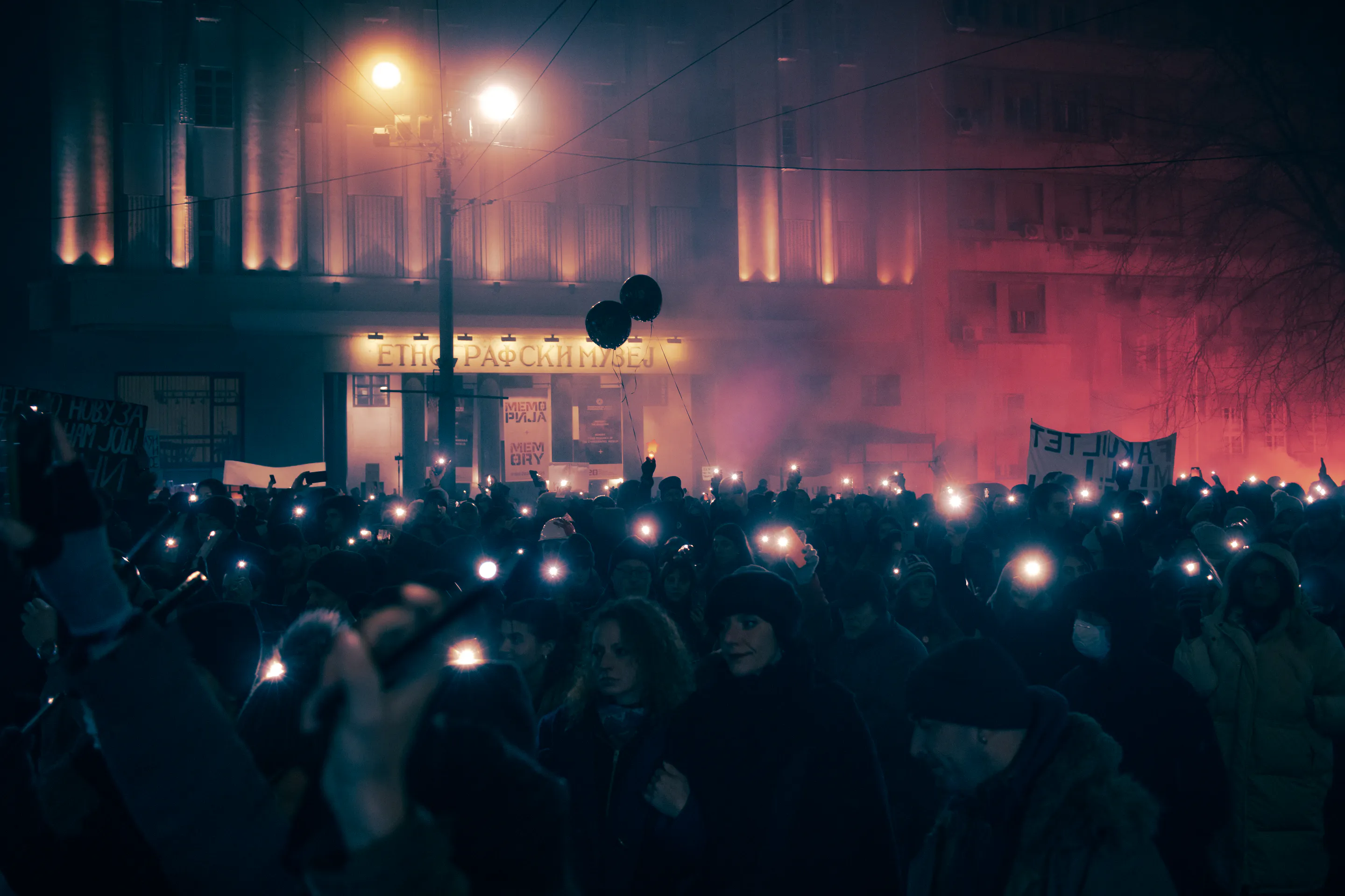 Red flare smoke washing over the protest beside the museum, black balloons above