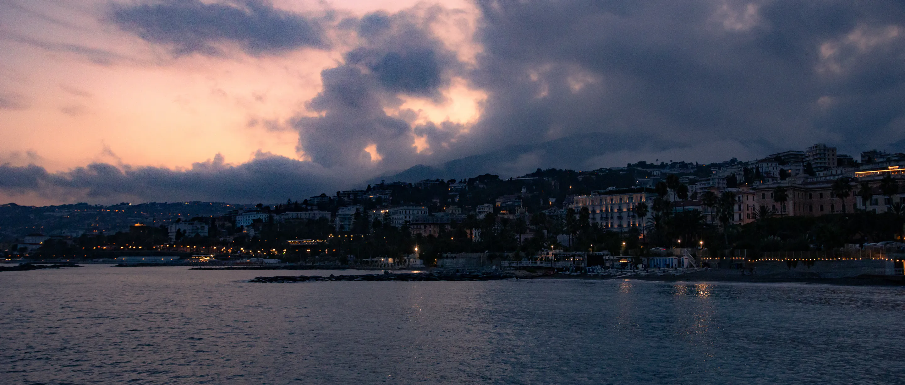 Town lights coming on around the curved bay under storm cloud