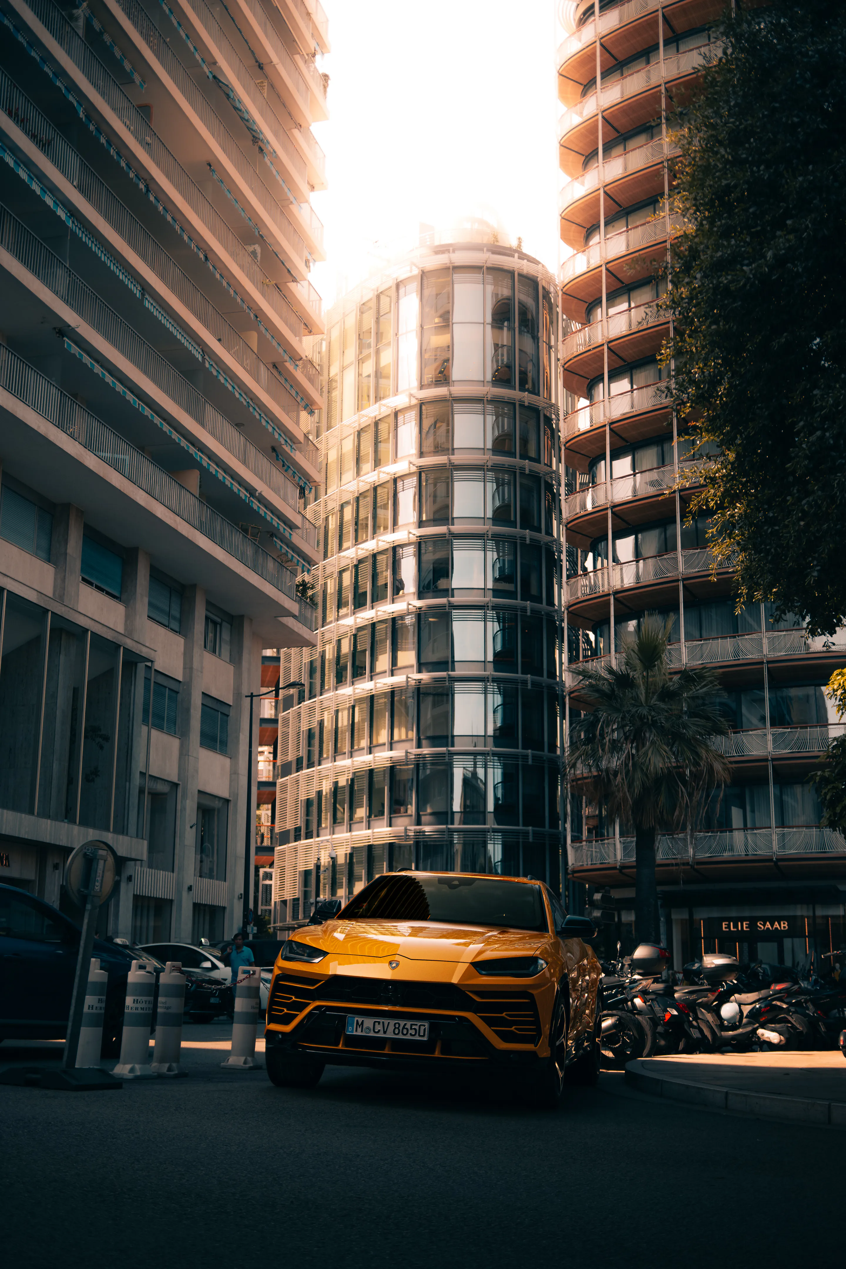 Yellow SUV between a curved glass tower and old stone, backlit by flare