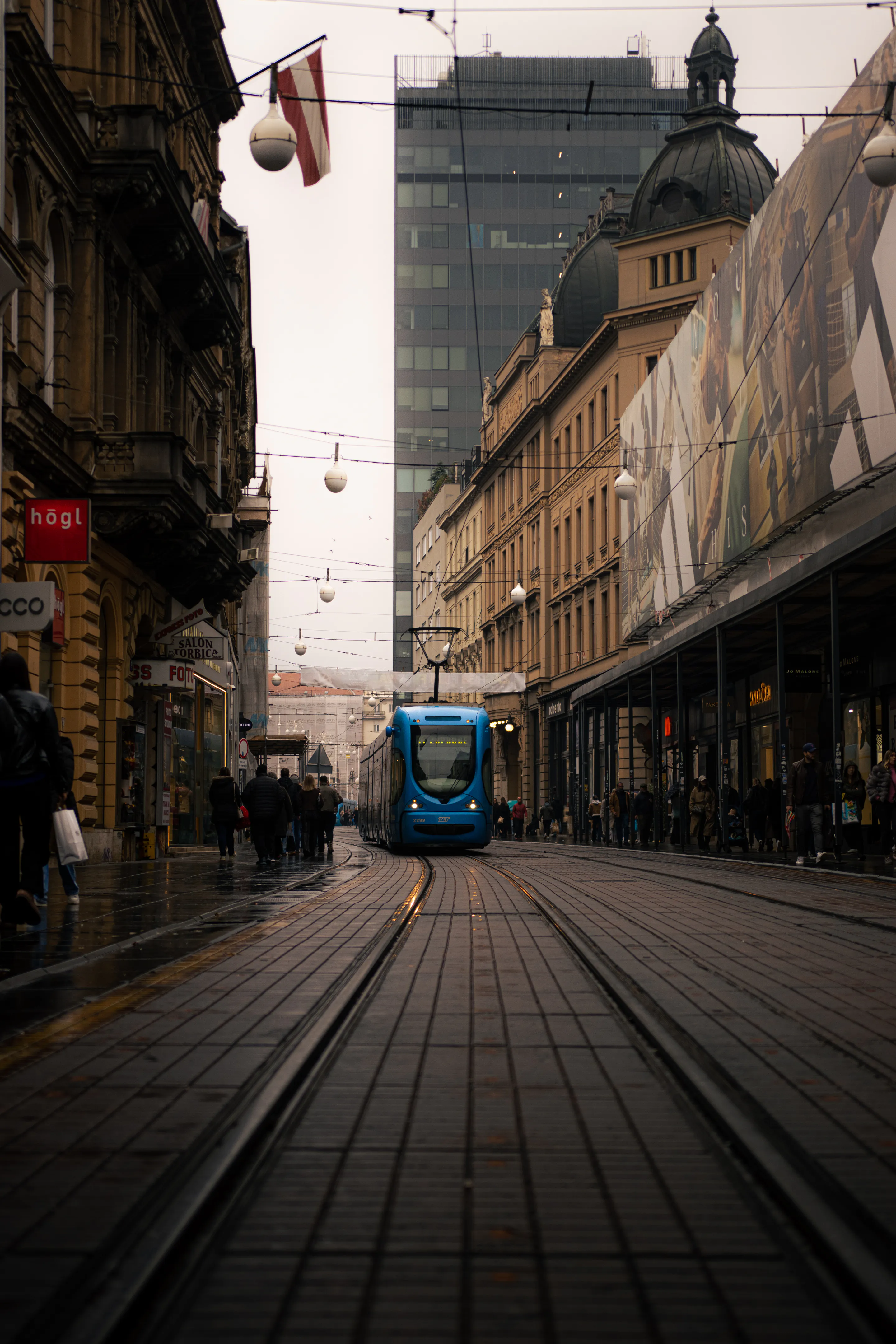 Blue tram descending the converging cobbled street under a web of wires