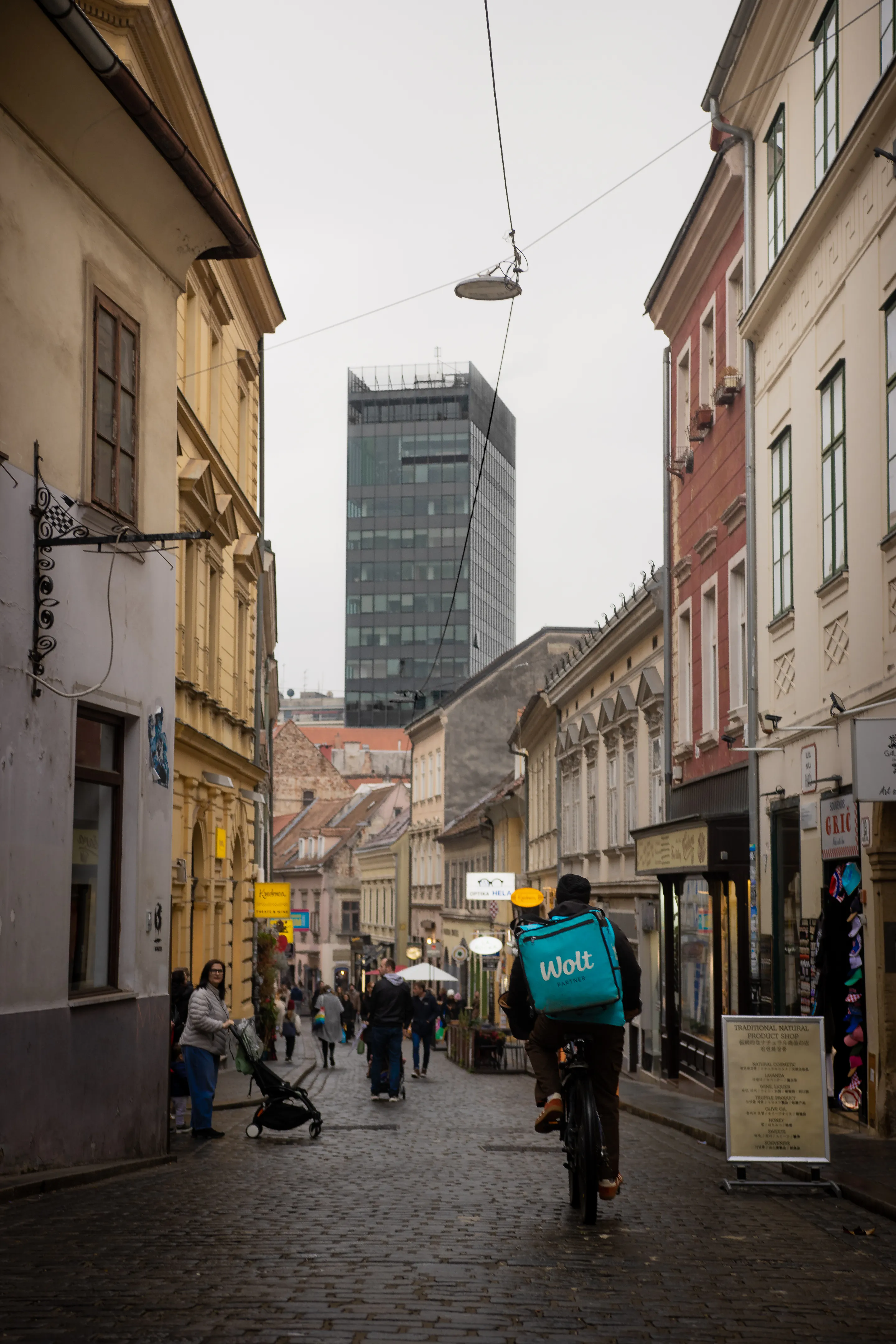 Delivery cyclist threading the alley toward the distant glass tower